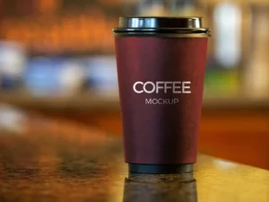 Dark-themed coffee cup mockup on a table with realistic lighting and shadows for branding design presentation.